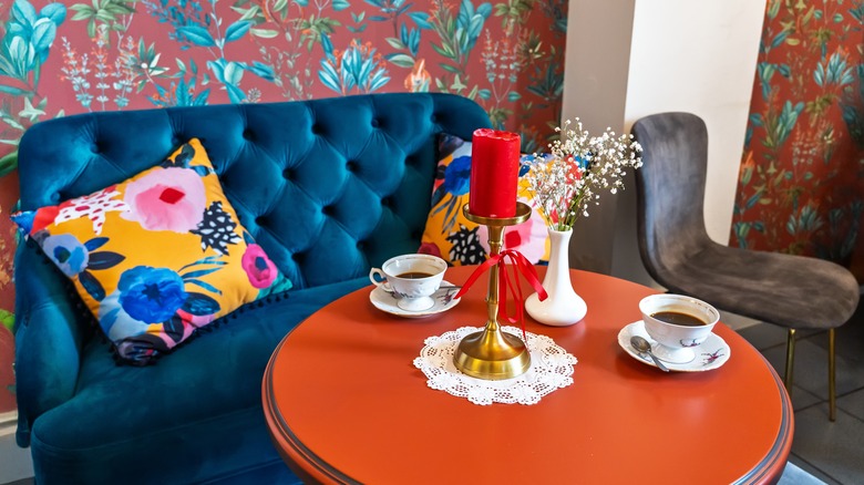 A bold living room space with patterned wallpaper, a big colorful couch, and an orange side table