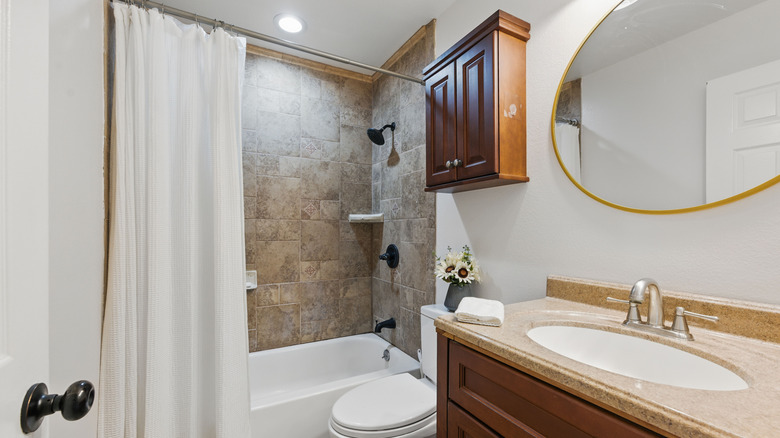 A bathroom with dark wood vanity, white toilet, and white shower curtain