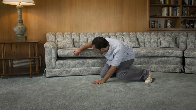 A man lifting a couch cushion to inspect the platform underneath