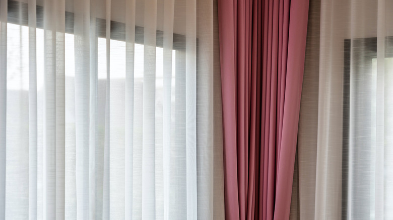 Sheer white and soft pink curtains drape over a lit window.