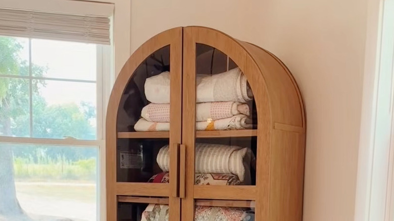 wooden thrifted cabinet storing blankets by window with lifted shades