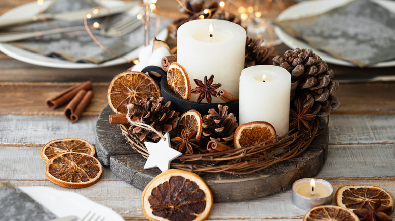 Minimal modern holiday decor with candles, dried orange segments, cinnamon sticks, and pinecones on a tray