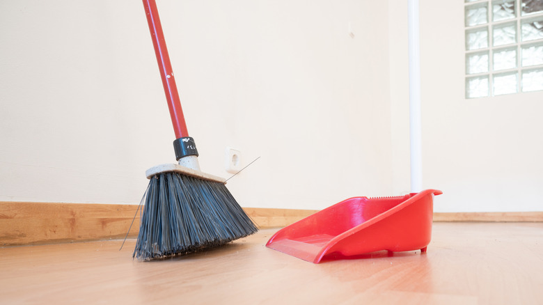 a broom leaning on the wall, next to dustbin.