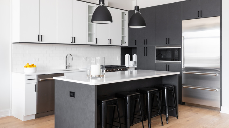 A modern kitchen with dark grey and white cabinets, stainless steel appliances, and black barstools.