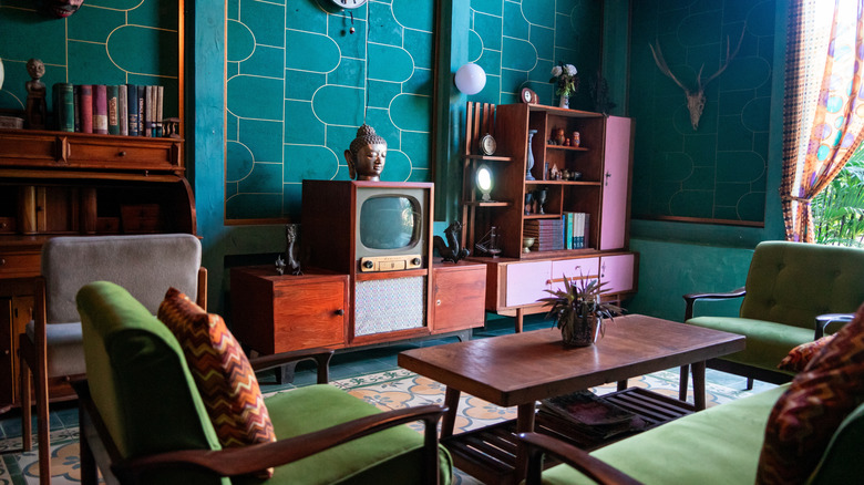 Eclectic living room with green sofa, teal wallpaper and mid-century modern furniture