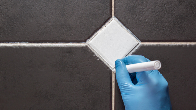 Gloved hand using grout pen on tile