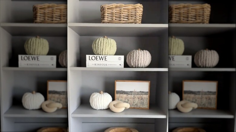 Screenshot showing three pumpkins covered in beige, white, and green yarn on a shelf with books