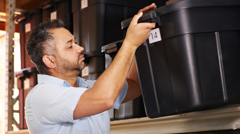 Man lifting plastic storage tote in garage