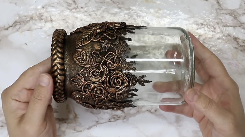 A glass jar covered with vintage-looking lace and clay flowers.