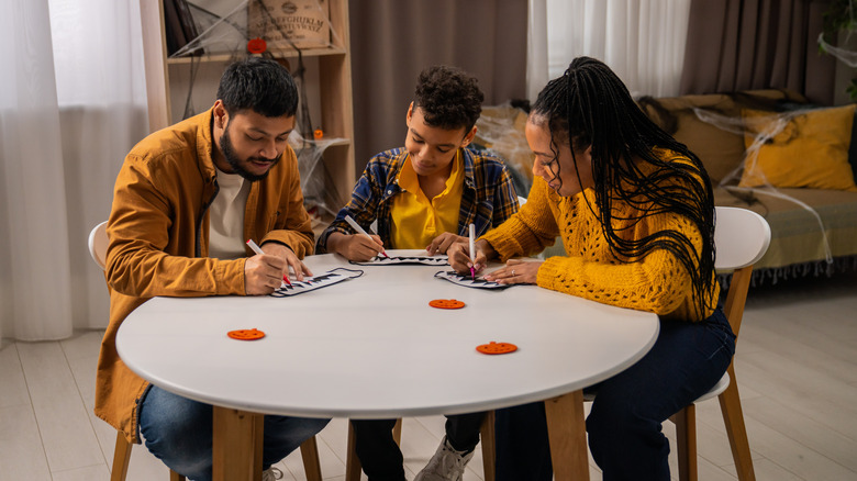 Family of 3 sitting at table making fall and Halloween crafts