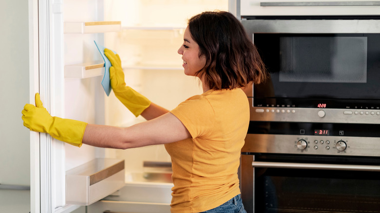 Smiling young woman cleaning the interior of a refrigerator