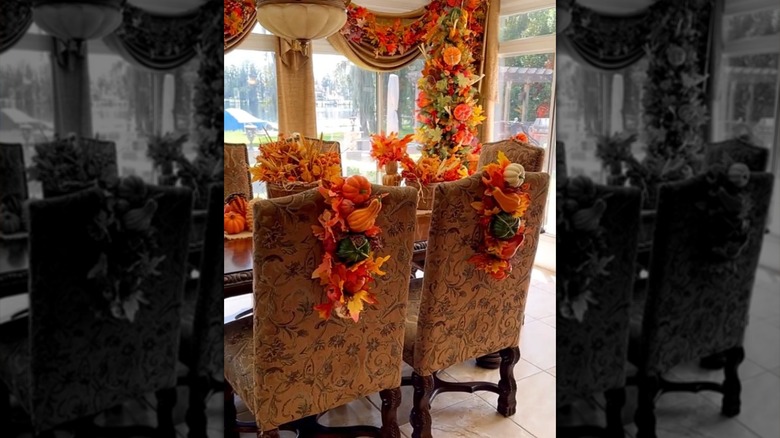 A dining room is adorned with fall decor including vertical wreaths hanging from chairs.