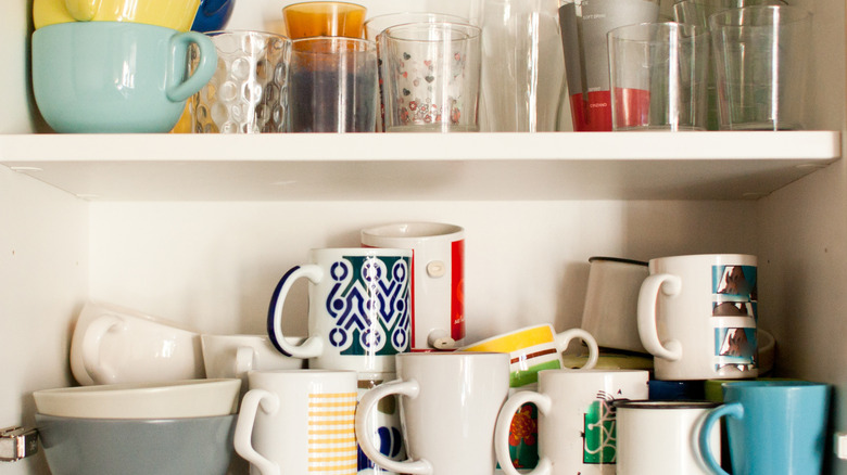 Cluttered collection of mugs and cups on a kitchen shelf