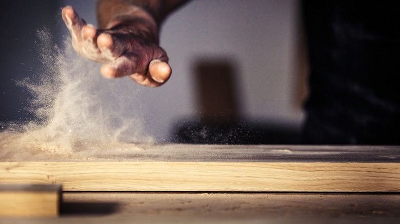 person working with dusty wooden plank
