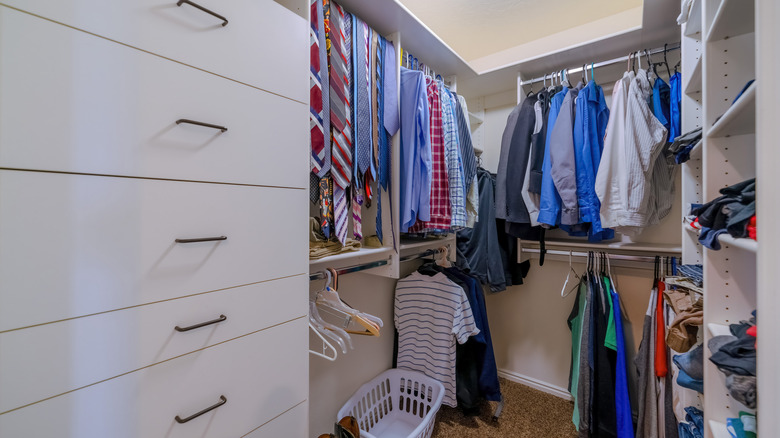 A small walk-in closet with drawers, shelves, and rods holding clothes