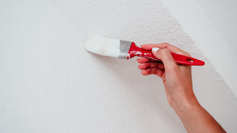 A person touches up white paint on a wall using a paintbrush