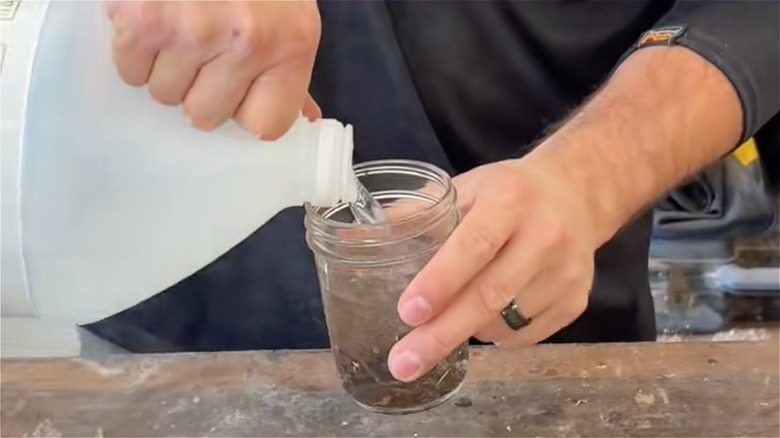 A man pours vinegar into a jar of rusty nails