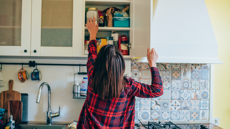 A woman reaches for a jar in her kitchen cabinet