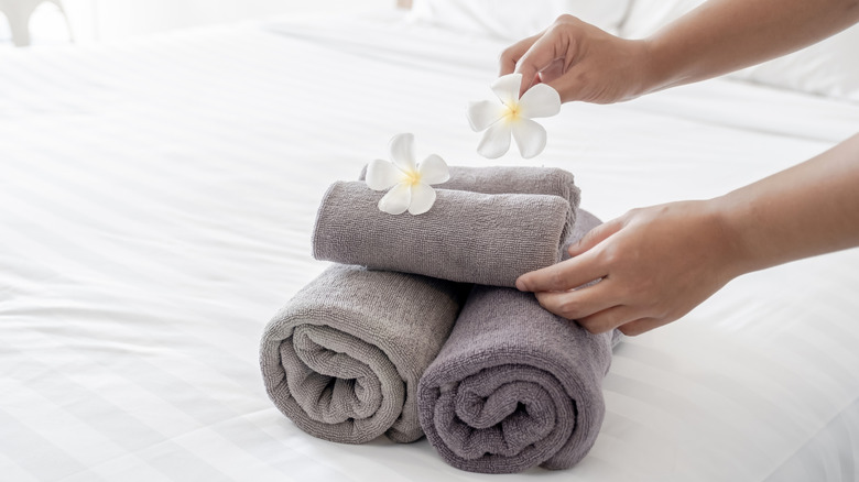 hotel maid placing rolled towels and single flowers on a bed
