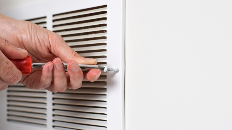 A person uses a screwdriver to remove an air vent for cleaning