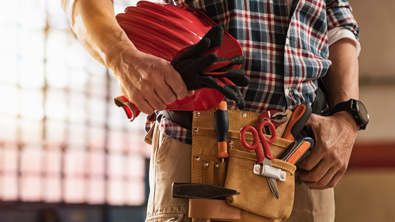 closeup of a man wearing a tool belt and holding hard hat ready for a renovation