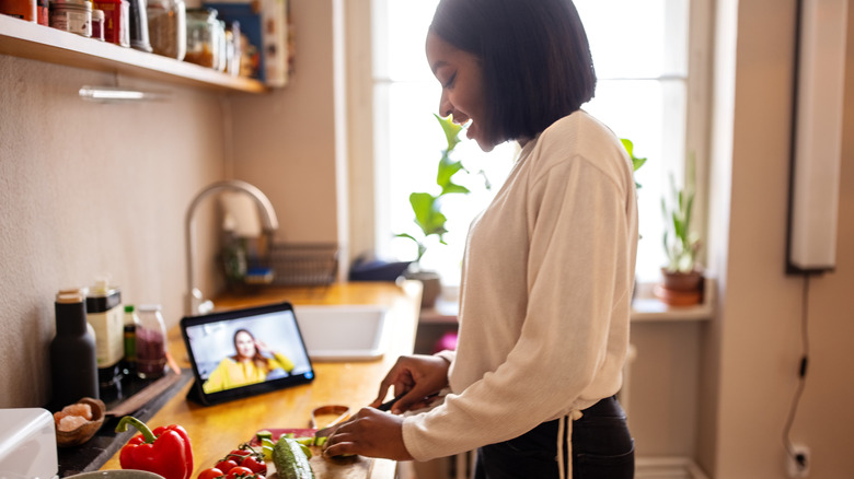 Woman cutting produce while on facetime call in kitchen