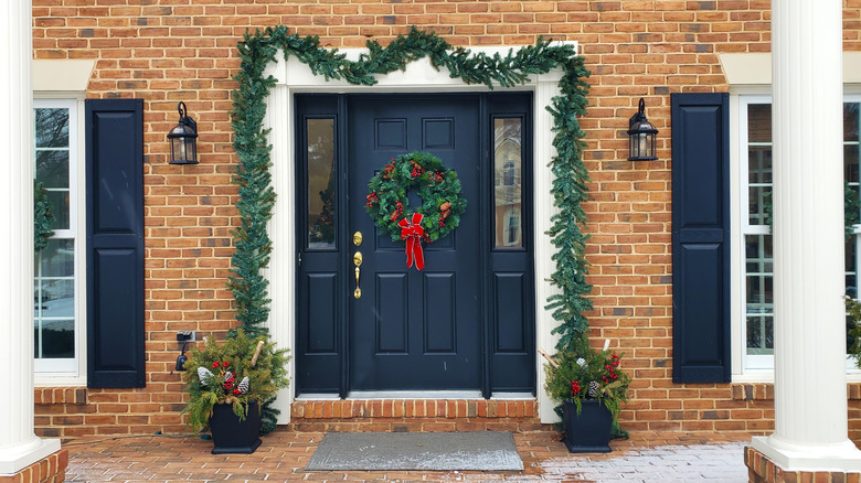 Brick home decorated for the holidays with wreath, garland, and potted evergreens.