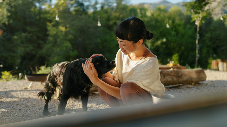 A woman smiling while petting her dog.