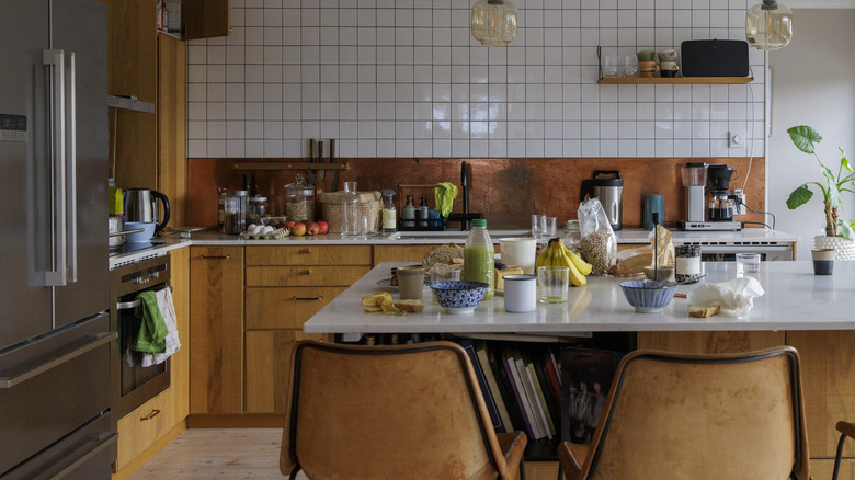 A cluttered kitchen island with bowls, fruit, and cereal