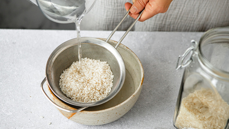 Close up of wtaer pouring over rice in a strainer over a bowl