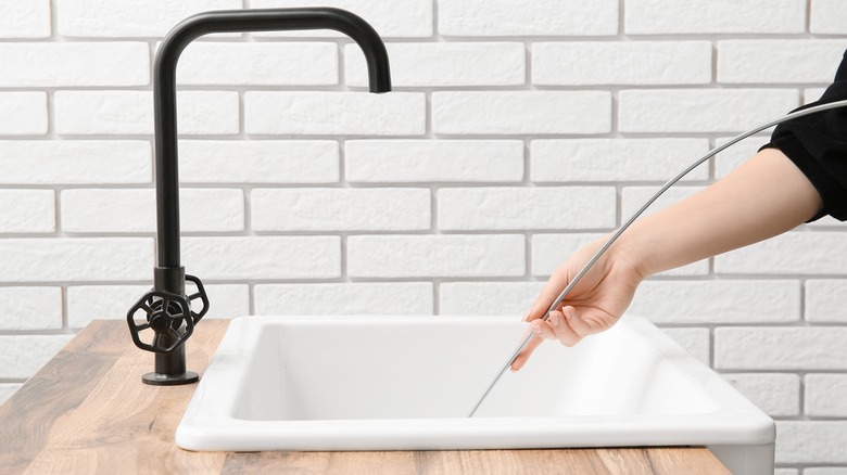 Person inserts a mechanical pick-up tool into a sink drain.