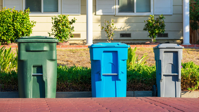 Three trash cans in front of a house.