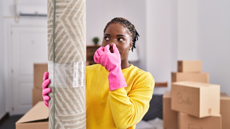 Woman holding nose at rolled-up carpet