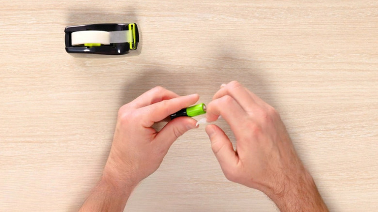 Man tapes the terminals of a battery with transparent tape for safe storage