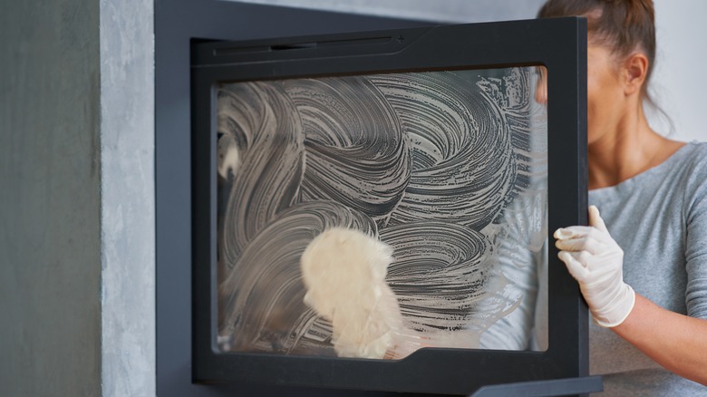 Person cleaning fireplace glass door