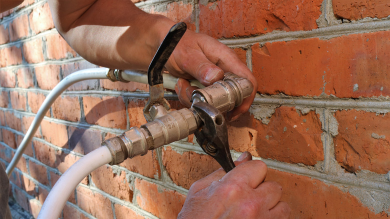 A person tightening garden hose connections on a brick wall with a single crescent wrench