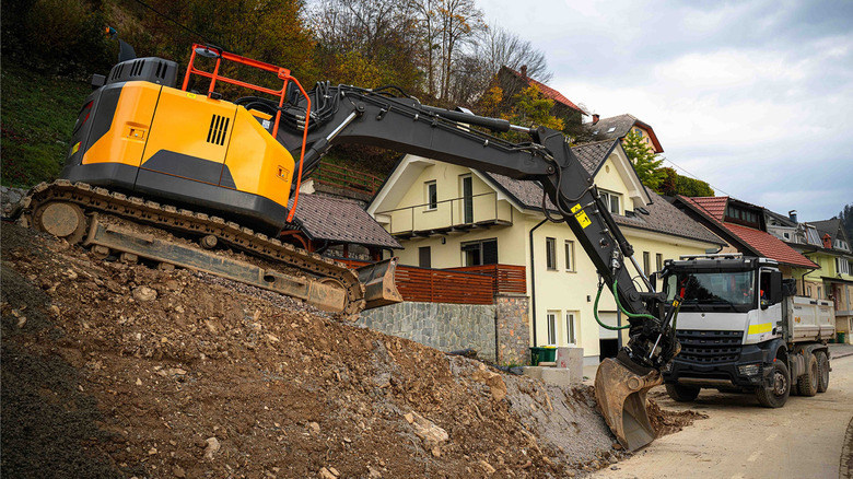 excavation work on a steep driveway features an excavator and a dump truck