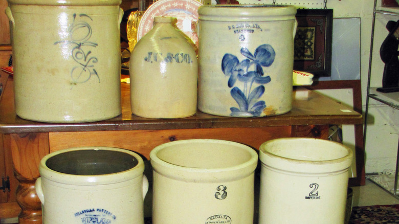 A collection of six antique stoneware crocks on a shelf, some with cobalt blue decorations.