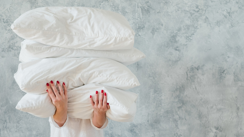 woman holding stack of large white pillows