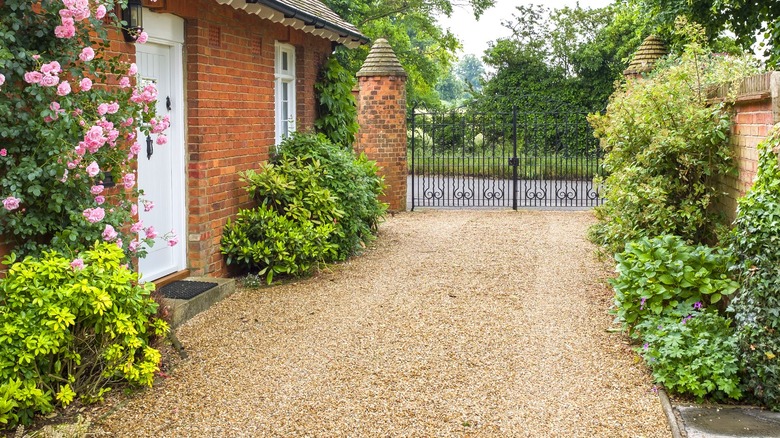 Pea gravel private drive behind iron fence next to brick house