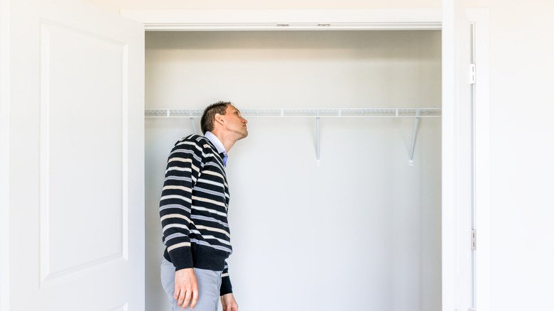 Man examines the closet doors from the inside, wondering if it would be easier to replace or just refresh them.