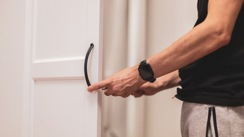 Man replaces the hardware on his closet door, switching it out for a modern black handle.