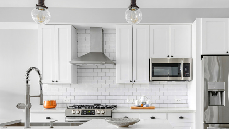 An all-white kitchen with white subway tile backsplash and stainless steel appliances.