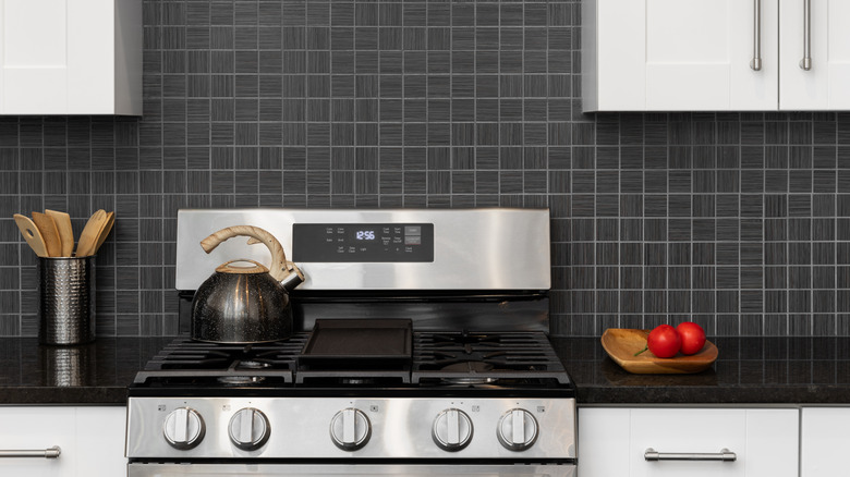 A stainless steel stove, white cabinets and black backsplash