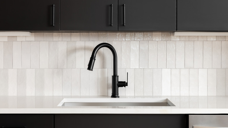 A modern kitchen with a black faucet, black cabinets and a white tile backsplash.