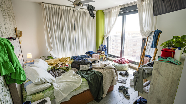 Cluttered bedroom with clothes on floor and bed