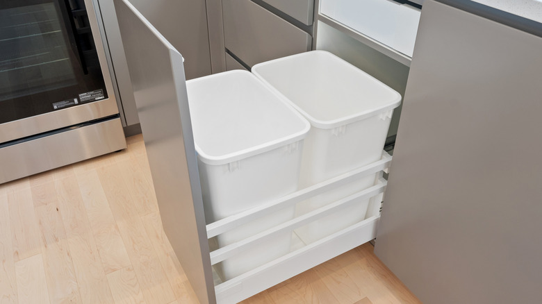 Two white trash cans in a silver cabinet