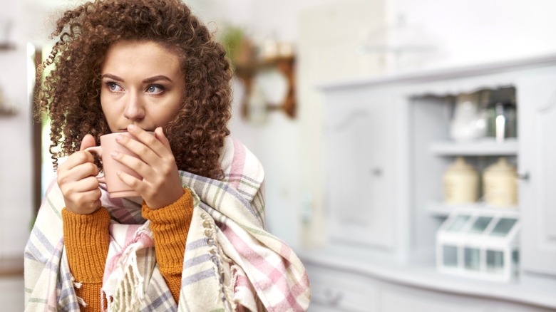 Woman wrapped in blanket while drinking tea to stay warm in home