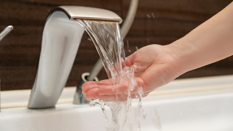 A person testing the temperature of water from a tap