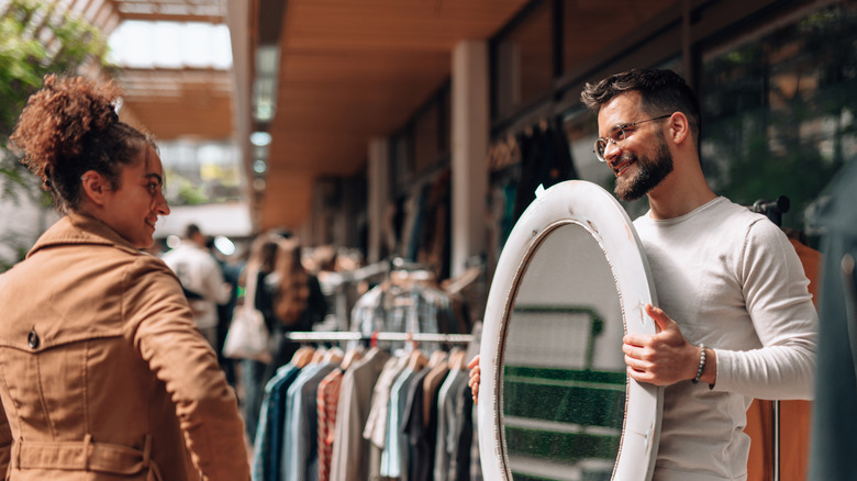 A man shows a woman an antique oval mirror at a store.